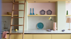 pastel-toned kitchen with yellow cabinets and pink walls. A sliding wooden ladder is connected to the wall
