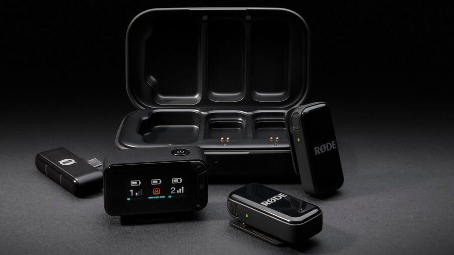 A RØDE Wireless GO II dual-channel microphone system, including two clip-on transmitters, the receiver unit with an LCD screen, and a charging case, is displayed on a black background.