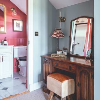 Dressing area with wooden vanity and mirror leading onto en-suite with red painted walls and panelling