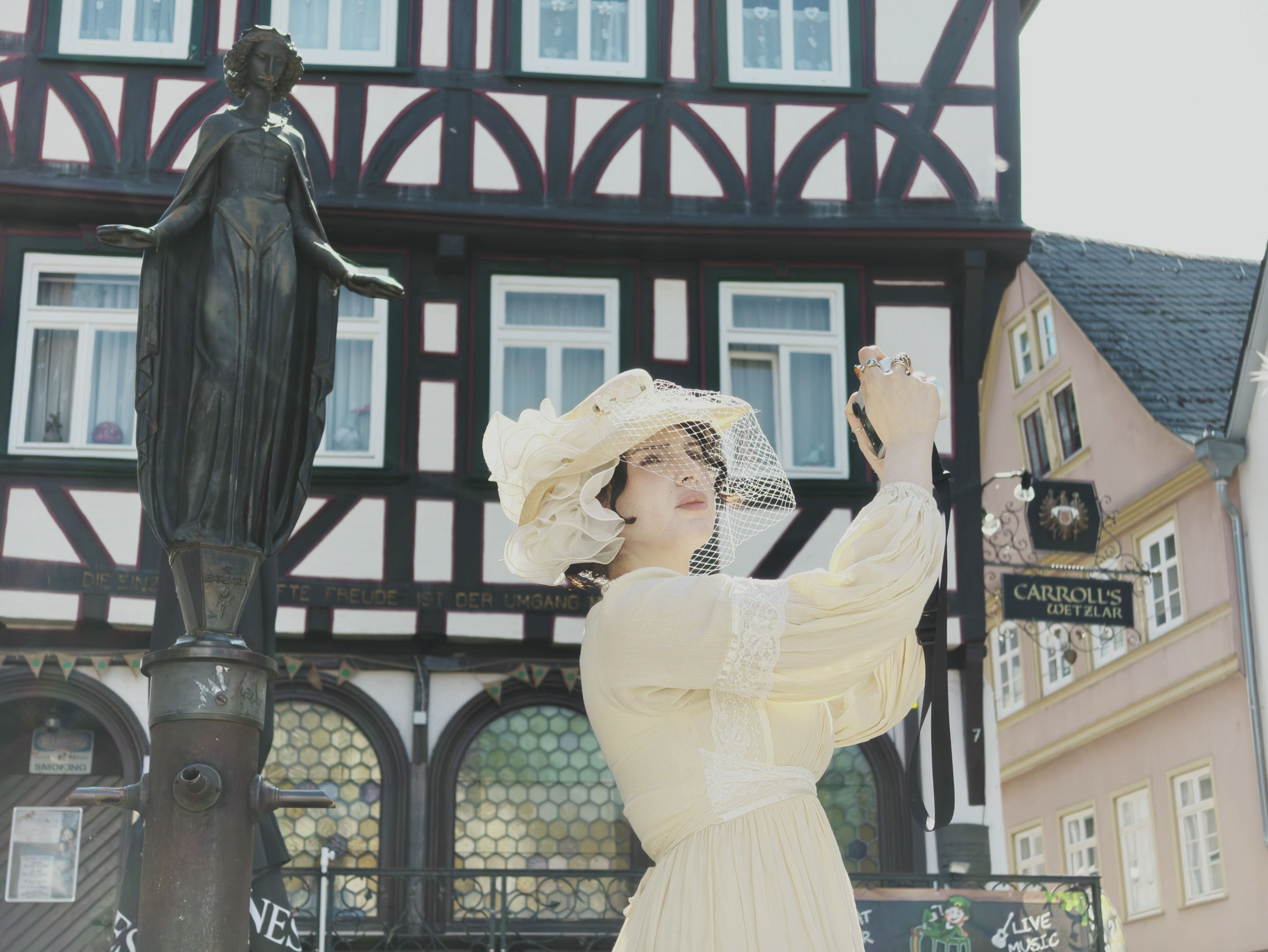 Insta360 Luna Ultra sample gallery: lady in period clothing holding a Leica camera, in quaint German town,