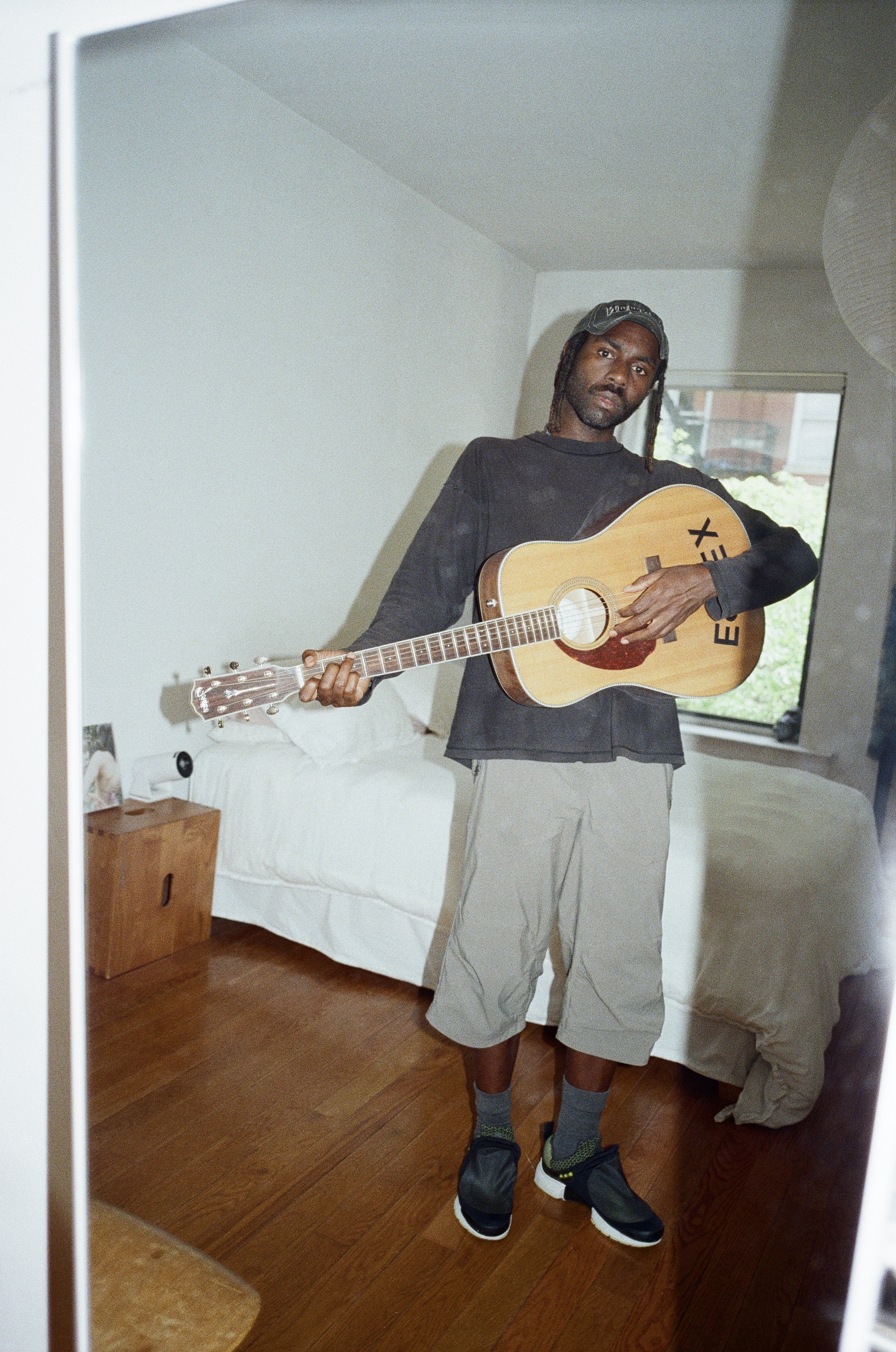 Dev Hynes standing with an acoustic guitar