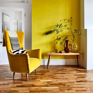 Yellow living room with wood flooring and yellow chair with black and white throw and cushion