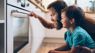 A father and son eagerly await something in the oven.