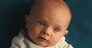 A Caucasian baby with blue eyes, lying on a dark blue background