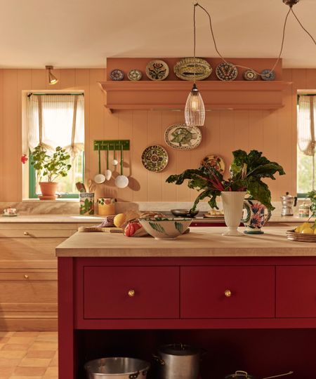 Kitchen with Fake Tan by Farrow & Ball painted walls, a red and marble island, walls of plates and vintage ceramics, and wooden drawers