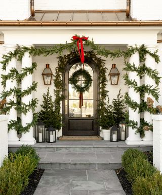 Porch decorated for Christmas with evergreen garlands and a red ribbon