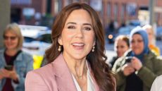 Queen Mary of Denmark, wearing a pink blazer and white waistcoat, smiles as she arrives at the Royal Danish Academy of Music