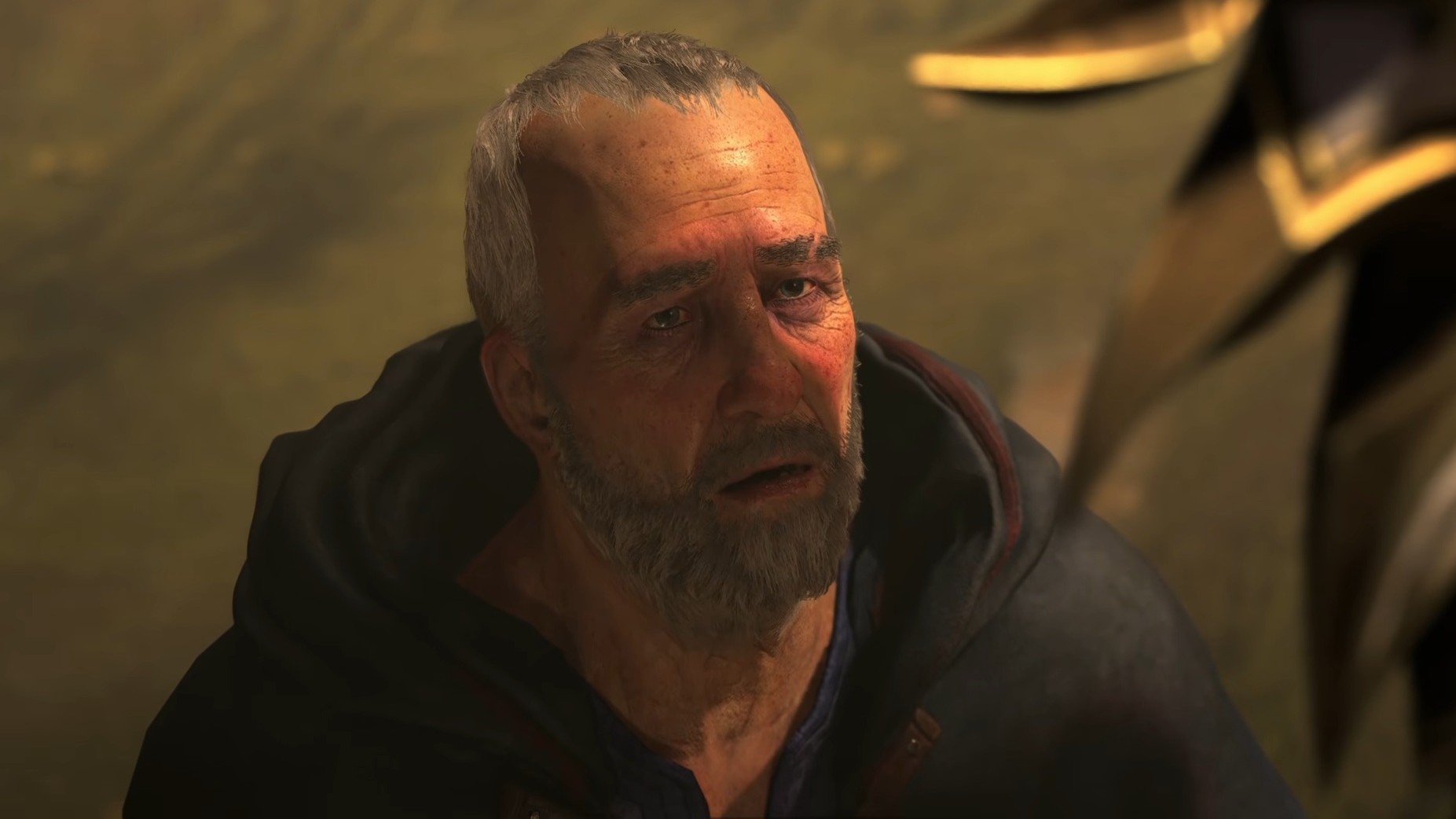 An older man with a gray beard looks up with a solemn expression. He is wearing a dark robe.