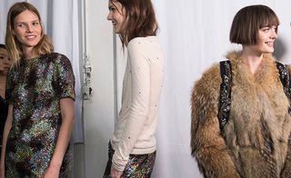 Three female models wearing looks from No 21's collection. One model is wearing a multicoloured sequin piece. Next to her is a model wearing a light cream top with dark spots and multicoloured sequin bottoms. And the third model is wearing a brown fur coat and dark coloured backpack with embellished straps