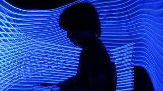 Silhouette of a child using a tablet in a dark room with blue lighting