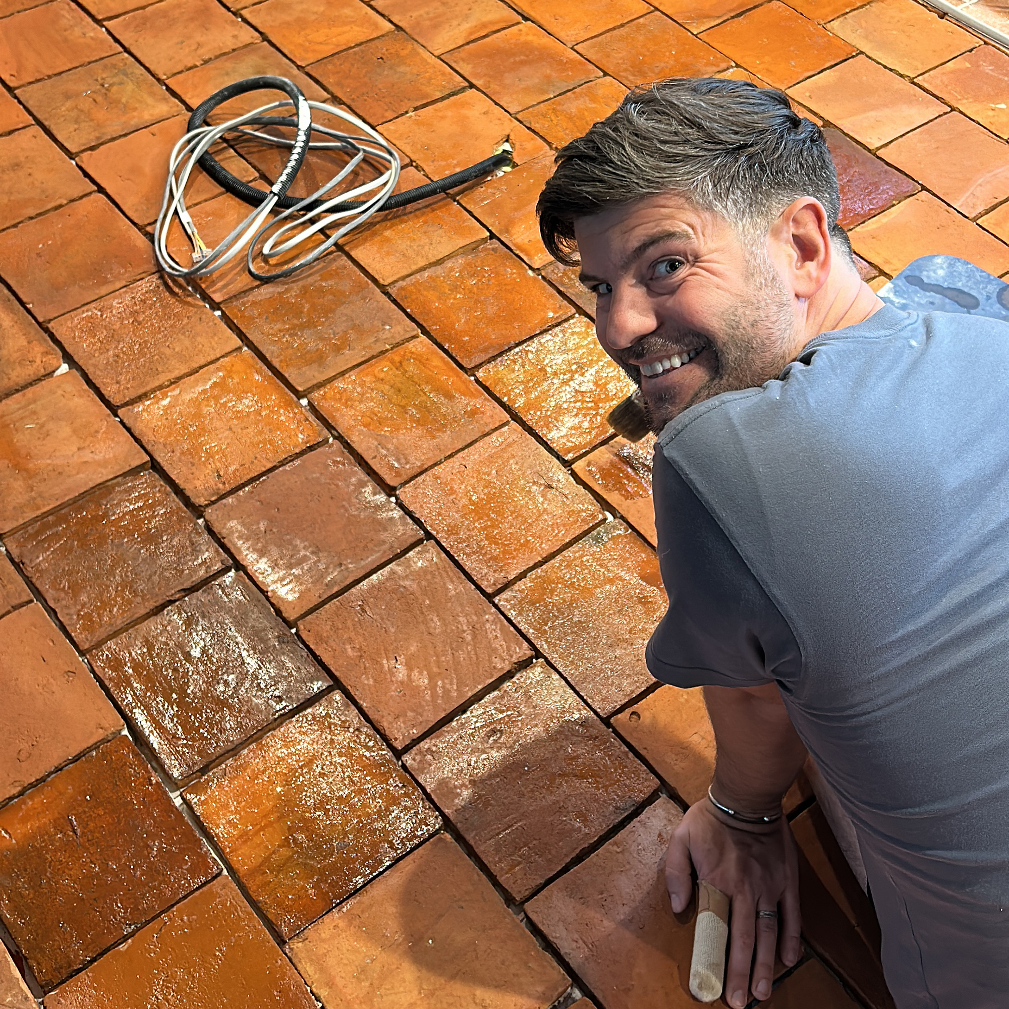 Andrew of the Home Boys kneeling on a wet terracotta tiled floor with lose wires on the floor in front of him