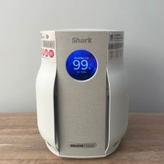 Shark BreatheClear Compact Air Purifier with NeverChange6 sitting on a wooden unit in front of a grey wall