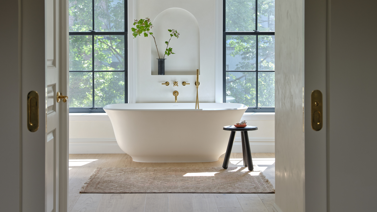 a beautiful sun soaked room with a white freestanding tub between two huge windows