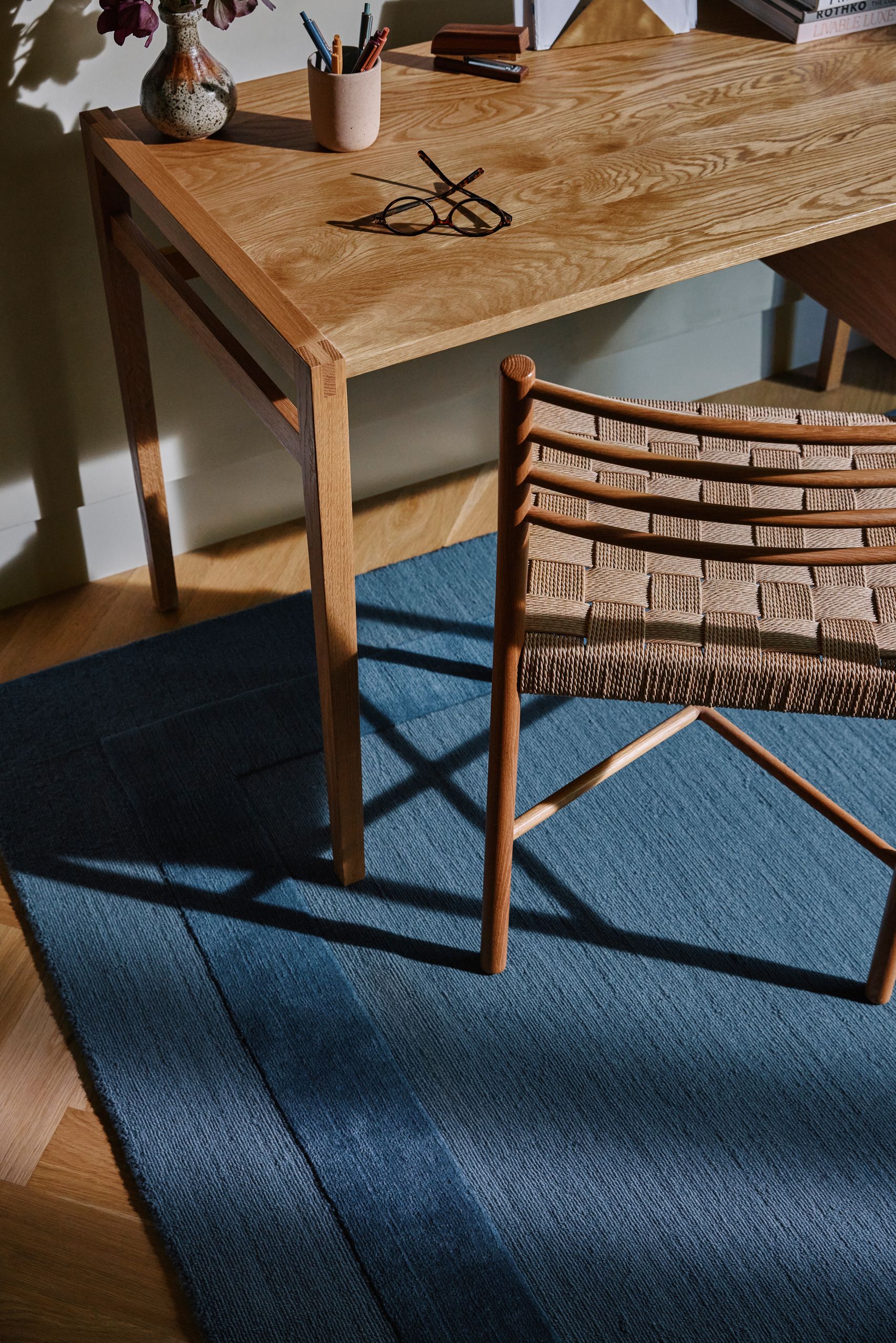 Overhead image of a wooden desk with a wooden chair on top of a dark blue rug.