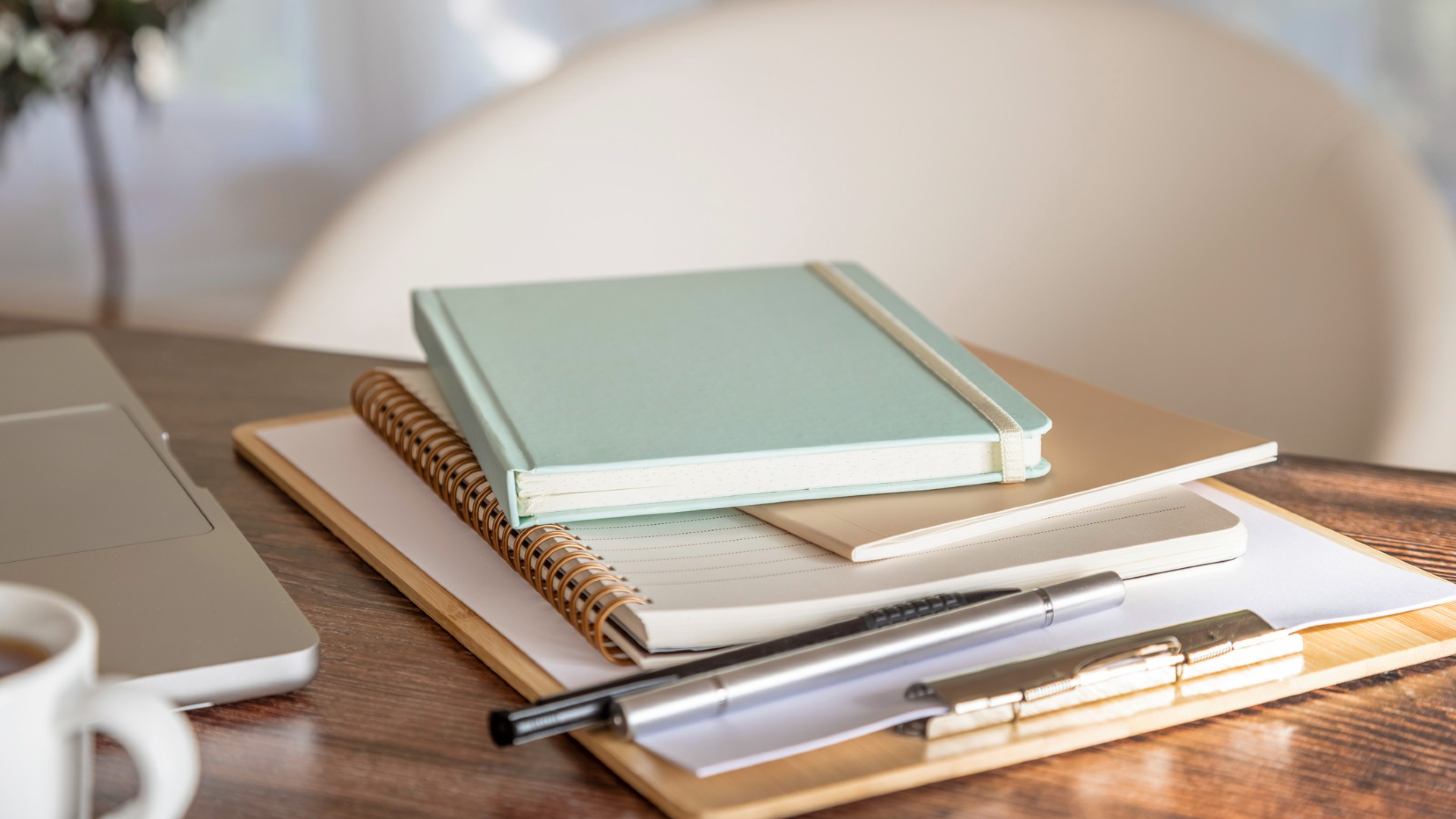 stacks of paperwork and diary and notepads on a desk with laptop and mug to the left