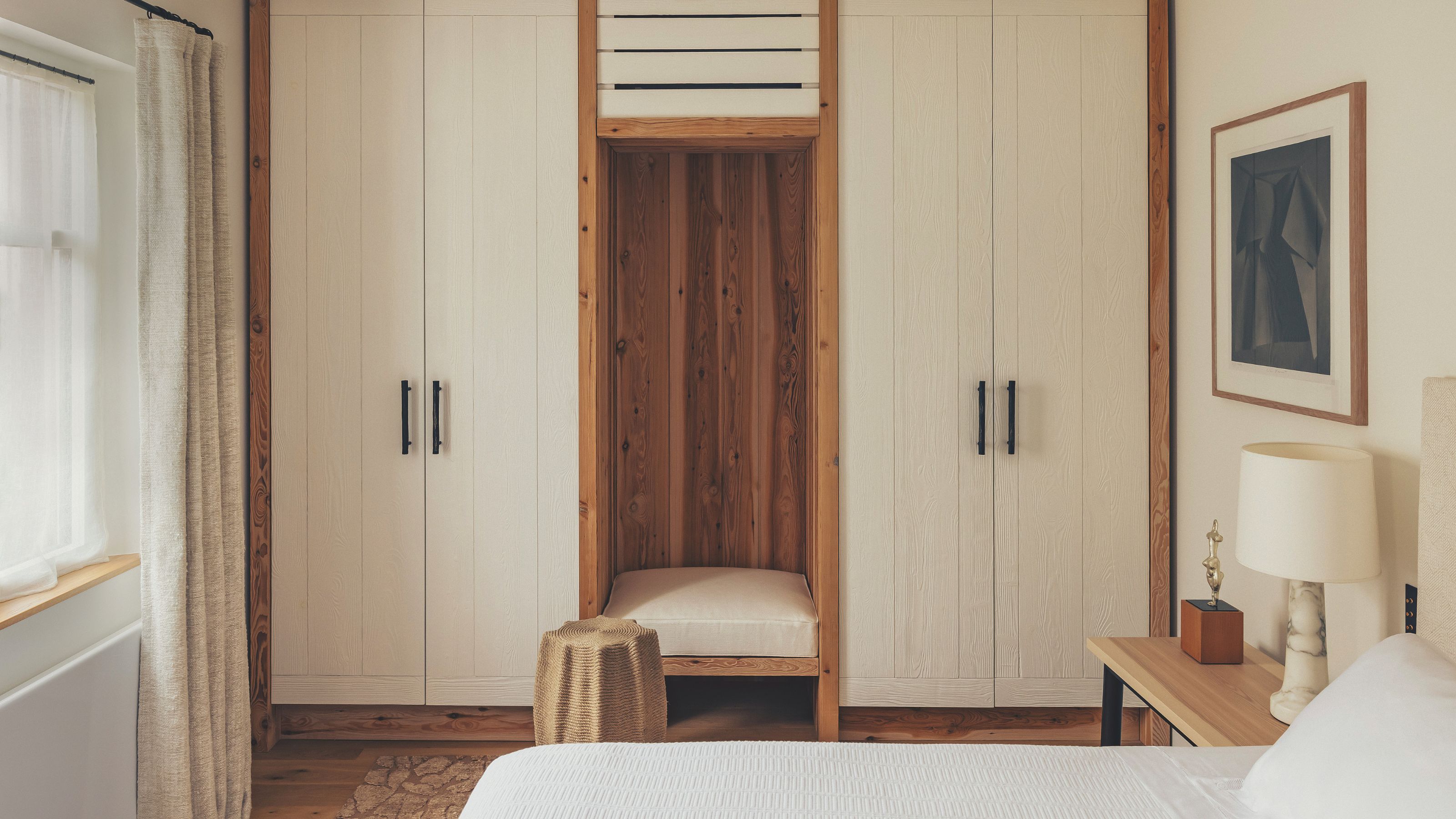 a rustic beamed bedroom with custom wooden cabinetry, a small built in set and neutral bed and linens