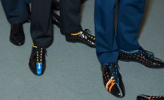 Lower leg view of two models wearing black formal shoes by Prada with pops of colour.