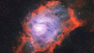 A nebula is photographed glowing in deep space among a sea of stars. It features a blue glowing core reminiscent of a lagoon, surrounded by red, flame-like clouds.