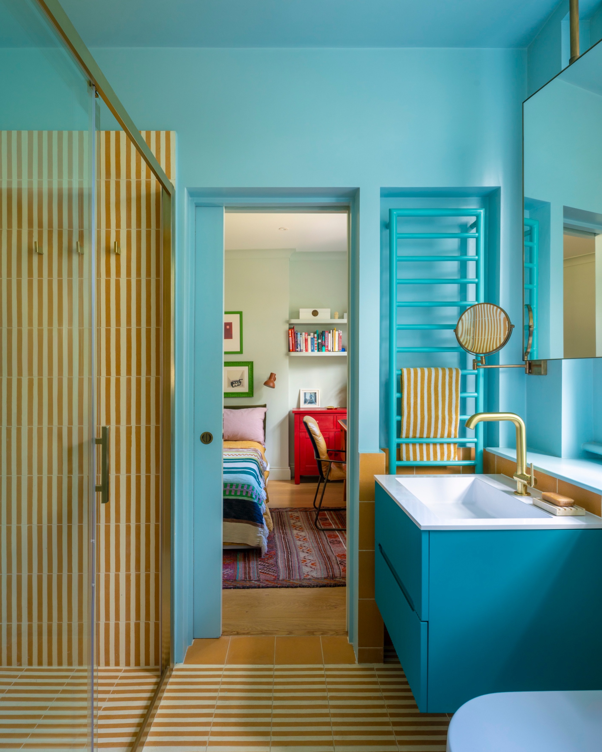 Bathroom with yellow-and-white striped tiles running across the floor and into a glass shower, aqua walls, a blue vanity and brass fixtures.