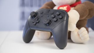 En svart Nintendo Switch Pro Controller står upplutad mot ett Donkey Kong-gosedjur på ett vitt bord.