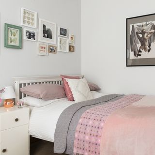 bedroom with white wall and white wooden bed with photo frames and blanket with pillows