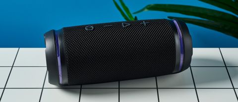 a black portable bluetooth speaker with LED panels sits atop a white table with a blue background