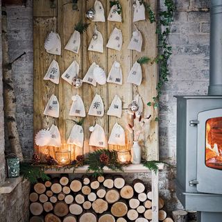 advent calendar on wooden backdrop with small bags, with a woodeburner to the right and a wood log pile underneath