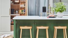 We love boho kitchen island ideas like this island with green cabinets, white countertop and three light wooden stools, and a marble vase with large green plant