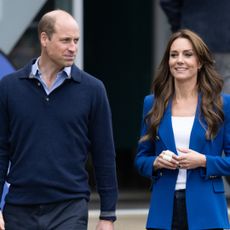Prince William wears a blue sweater and shirt, and Kate Middleton wears a blue blazer and white T-shirt, while Princess Diana wears a blazer adorned with pearls