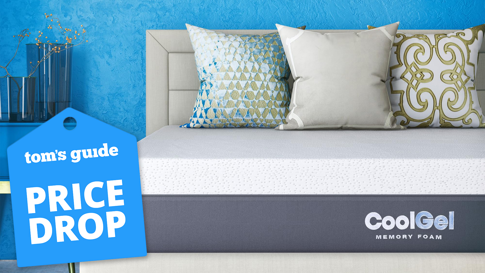 A close up of the Cool Gel Memory Foam Mattress on a bed frame in a bedroom, with three cushions resting against the headboard. A Tom's Guide Price Drop deals badge (left)