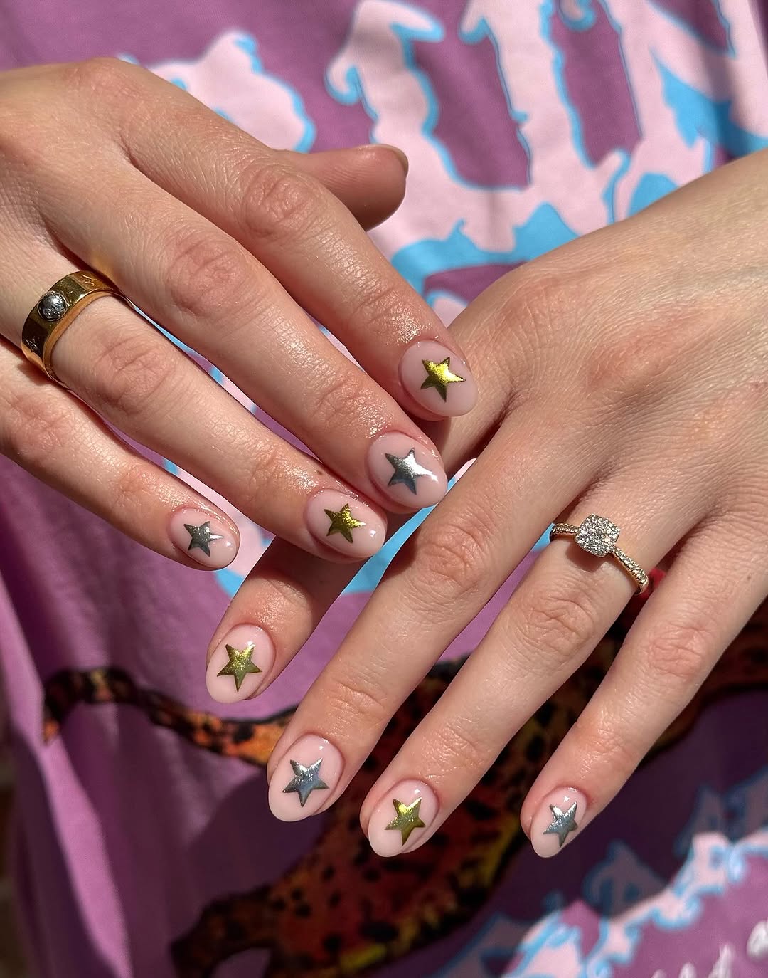 Close-up photo of a person&amp;rsquo;s hand showcasing a pale pink manicure on almond nails with tiny gold and silver nail stickers.