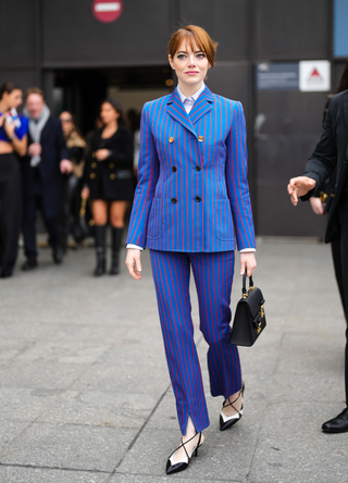 Emma Stone wears a white shirt, a royal blue with small red striped print pattern buttoned blazer jacket, matching royal blue with small red striped print pattern suit pants, a black shiny leather handbag from Louis Vuitton, black and white shiny leather pointed heels shoes , outside Louis Vuitton, during Paris Fashion Week - Womenswear Fall Winter 2023 2024, on March 06, 2023 in Paris, France