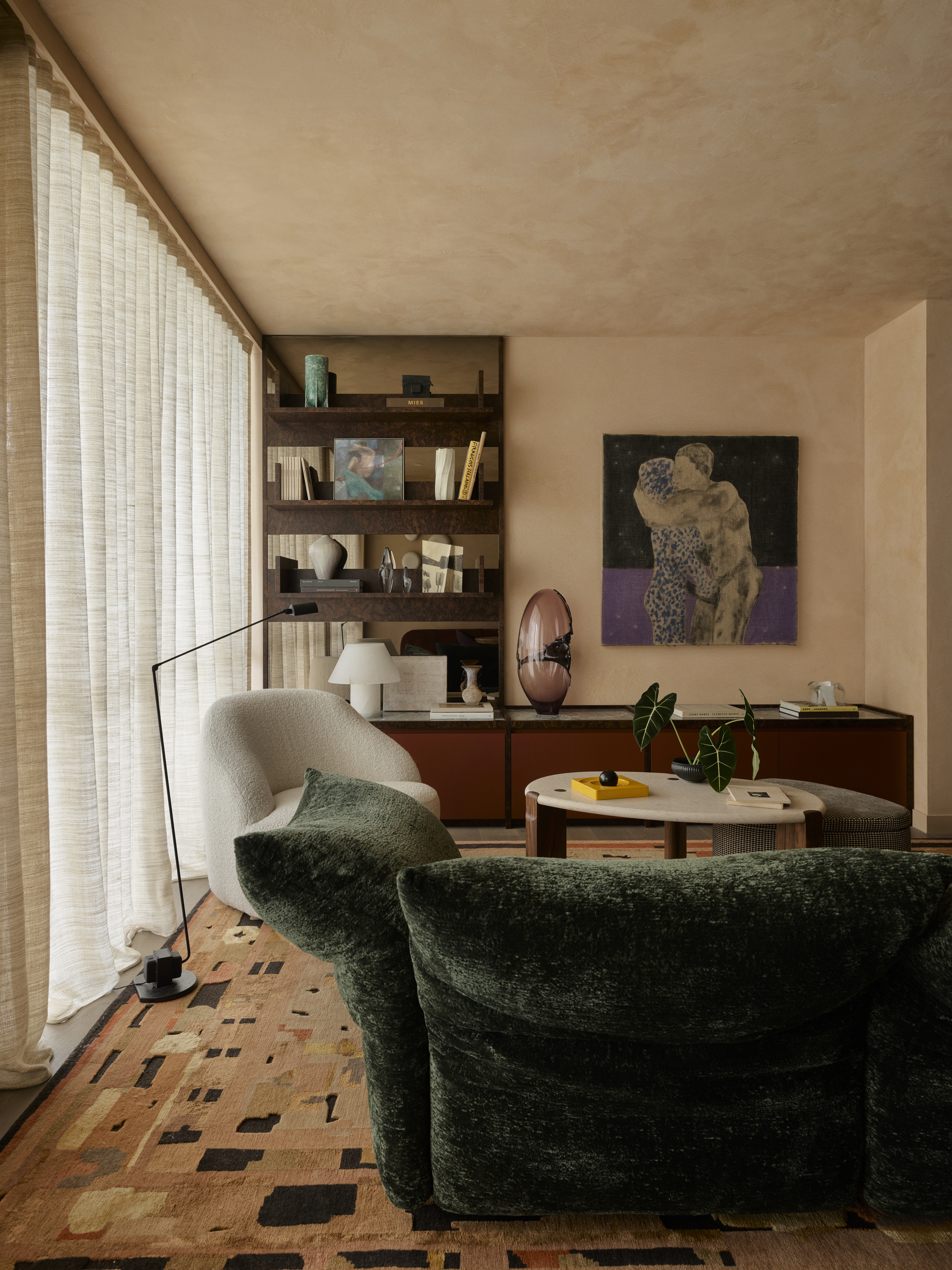 modern living room with green edra standard sofa, patterned rug, plaster walls and ceiling, sheer curtains, red entertainment unit, bookshelf, artwork and nesting coffee tables