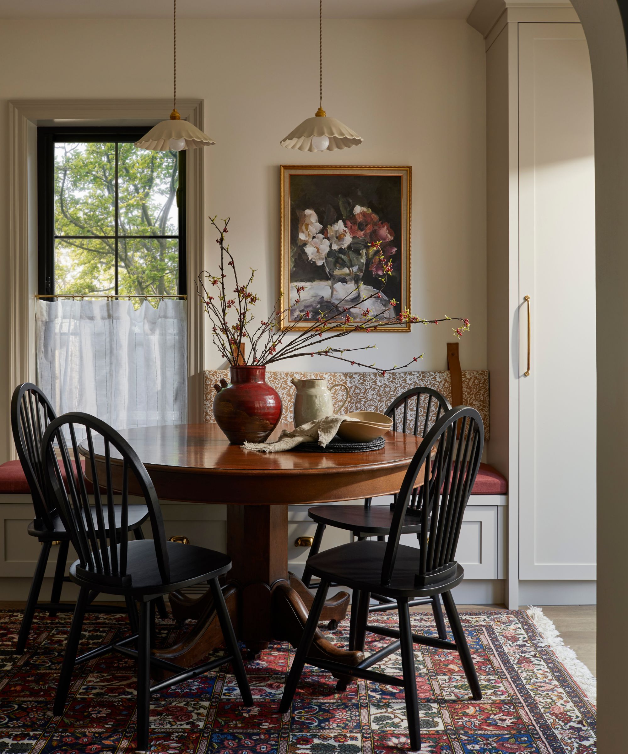 a warm beige dining nook with a banquette seat, a round wooden table, black chairs and a vintage rug