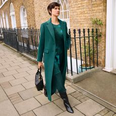 Model wearing a turquoise wool coat and dress sold at Phase Eight walking down a street