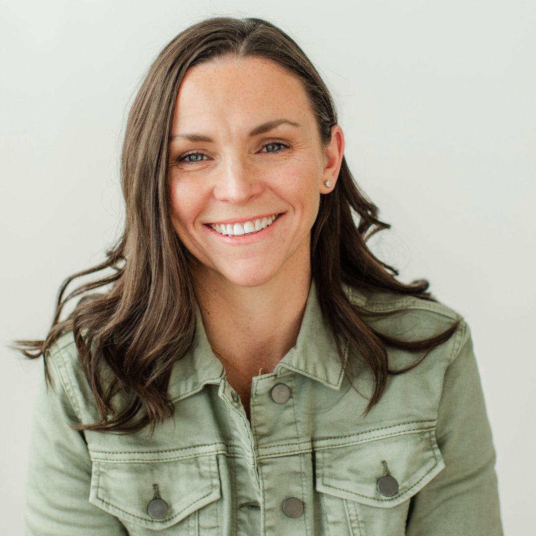 The image shows a dark haired woman wearing a sage green denim jacket smiling into the camera