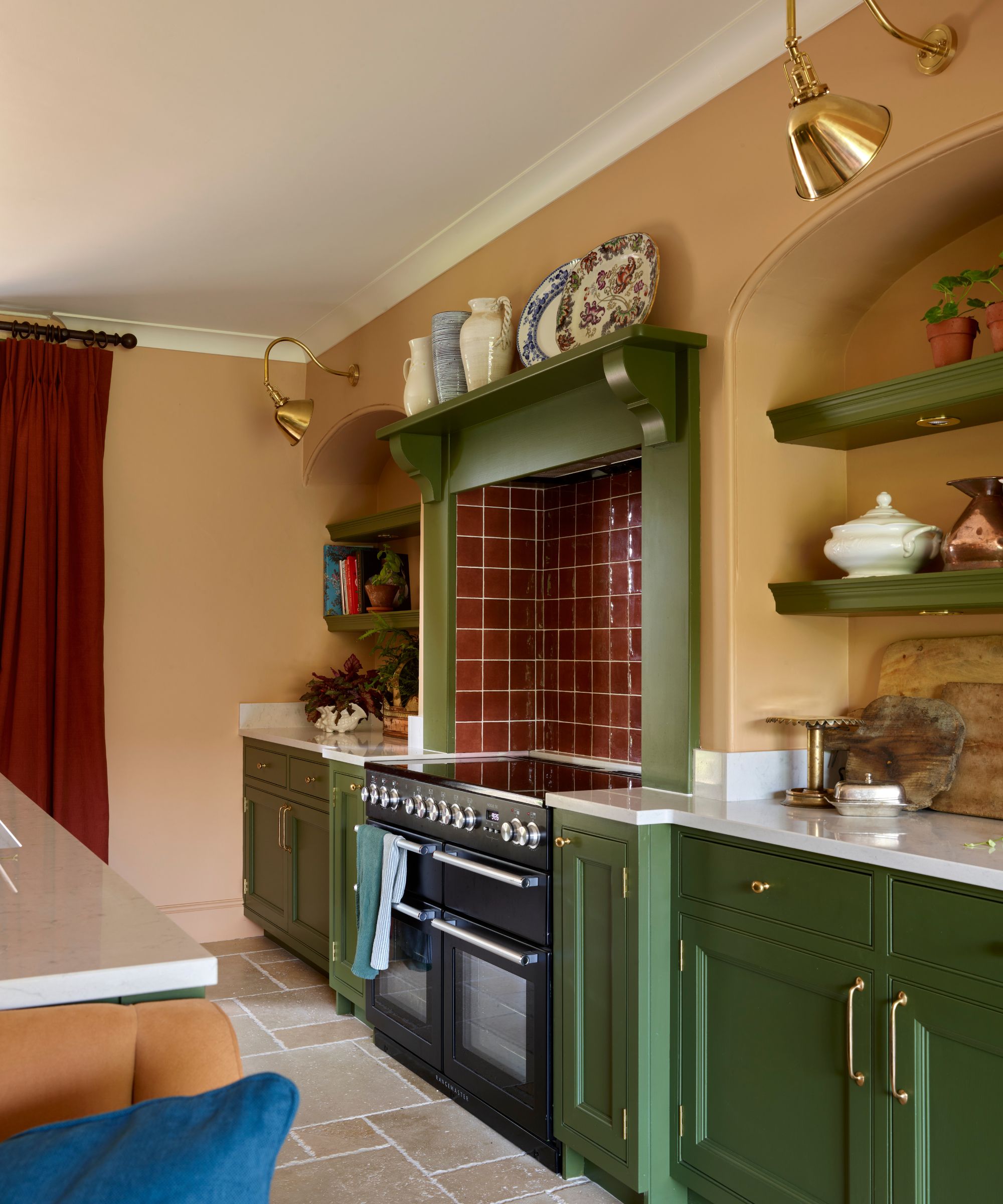 Kitchen with terracotta painted walls, dark green painted cabinetry, maroon tiled stove and ceramics