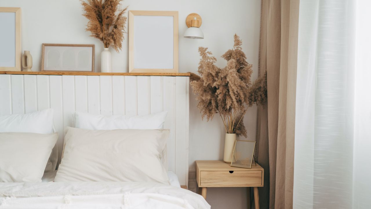 A neutral boho themed bedroom shot with white walls with natural elements like flowers and a wooden nightstand