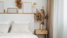A neutral boho themed bedroom shot with white walls with natural elements like flowers and a wooden nightstand