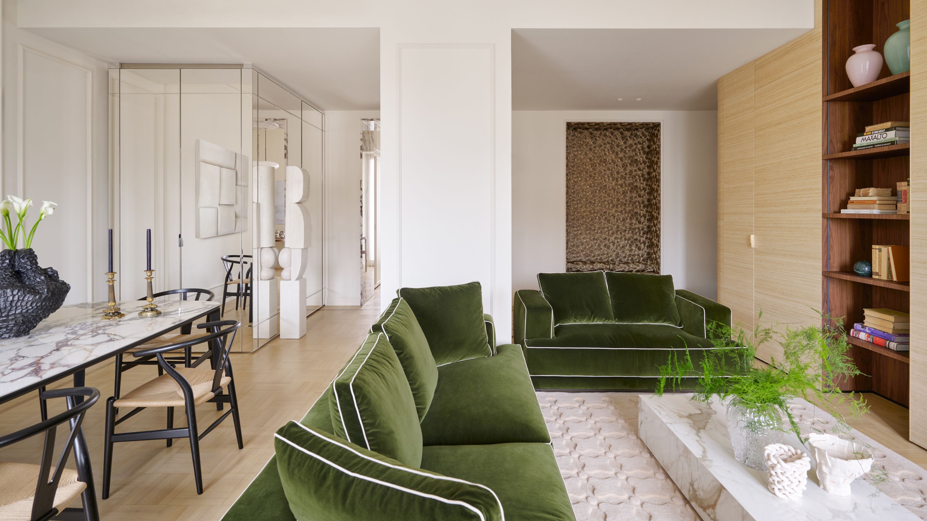 a white milanese apartment with open plan living dining area divided by a pillar and green velvet couches