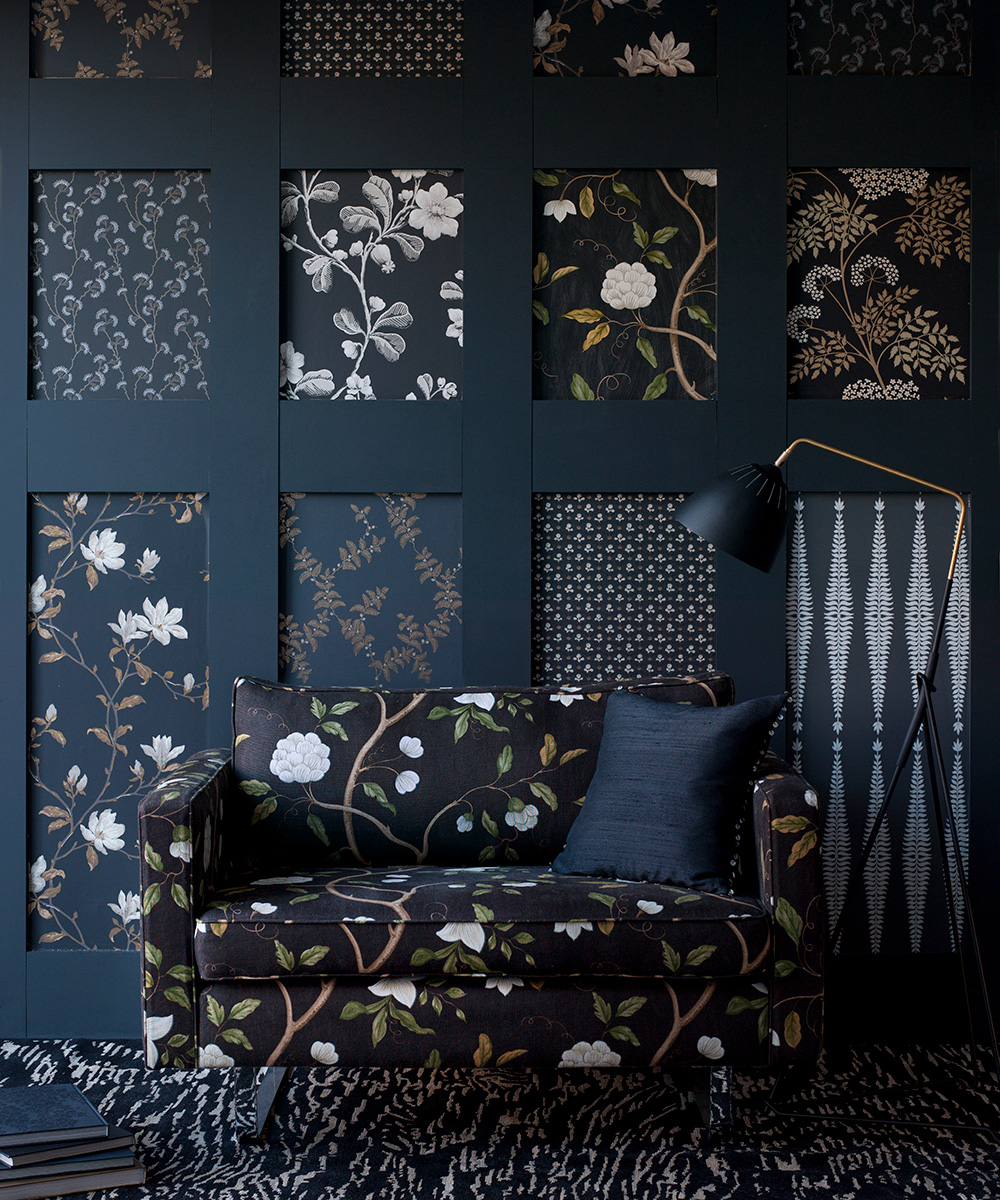 A black floral sofa in front of a black paneled wall with different dark wallpapers in each gap