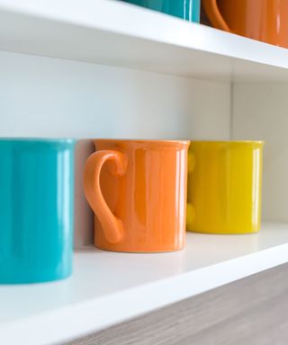A blue, orange, and yellow coffee mug lined up on a white shelf