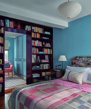 bedroom with blue walls, patterned throw, headboard and bookshelf