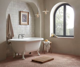 freestanding bath on pale brick terracotta floor tiles in bathroom with arch features and windows