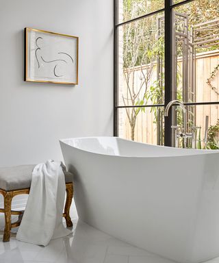 A modern rectangular white bath tub in front of a large window.