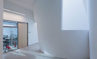 A curved white wall in the corridor of a building. on the left is the door that leads to a studio