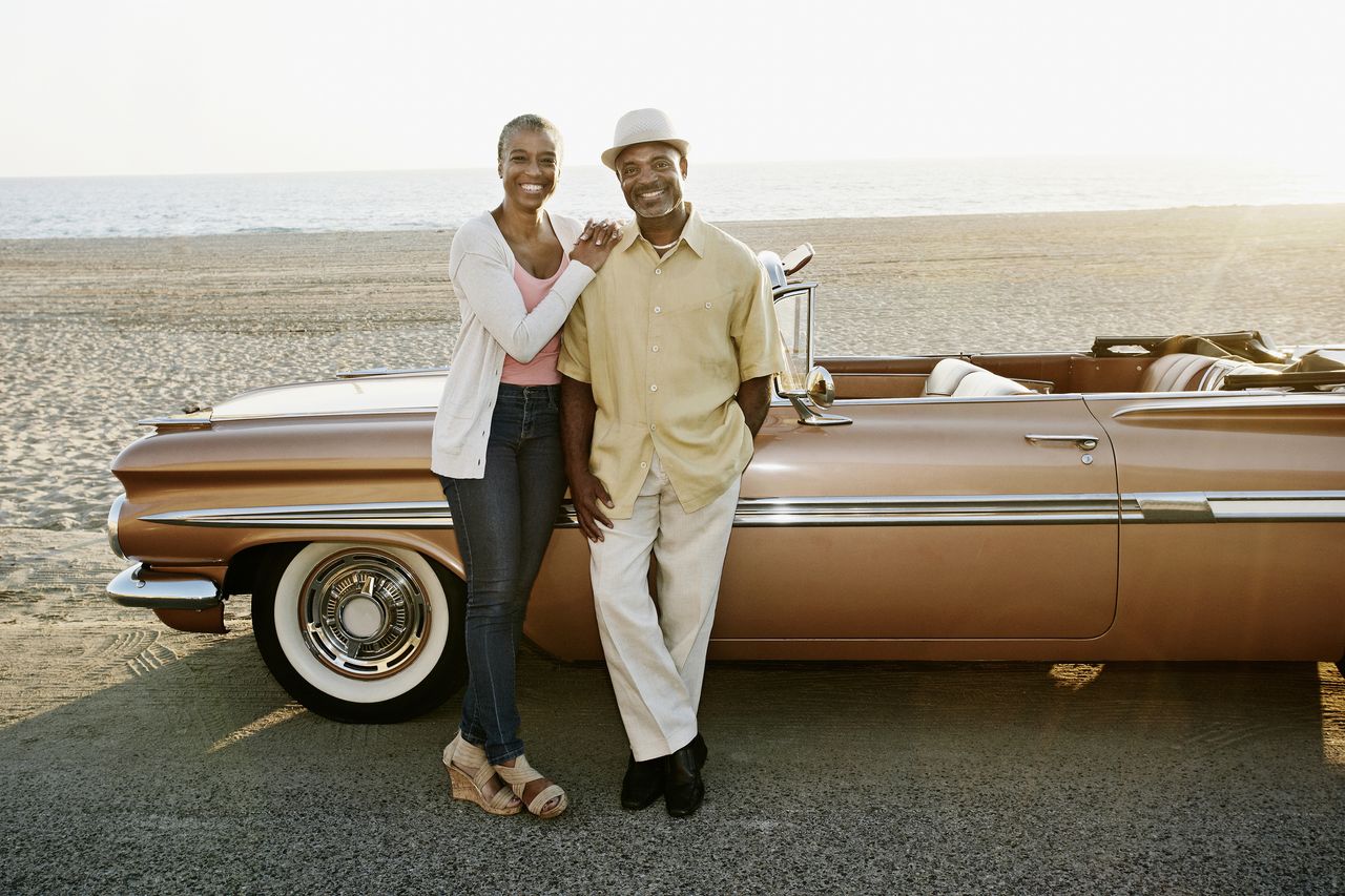 A retired couple poses in front of their classic convertible car.