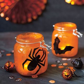 Spooky lanterns made from glass jars with spider and bat decorations on a black table