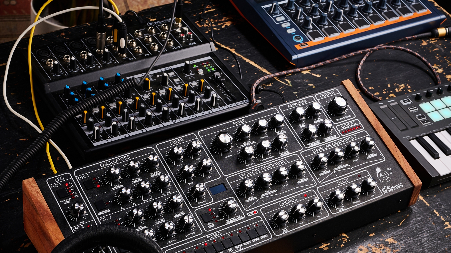 A selection of synthesizers, MIDI controllers, and a mixer on a wooden table