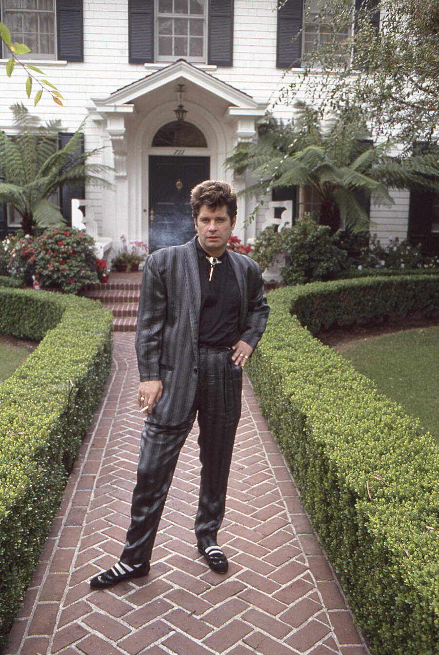 Ozzy Osbourne in a suit, standing in front of his house in Beverly Hills